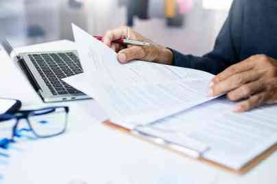 © stock.metket.com - stock.adobe.com Person mit Dokumenten und Laptop
